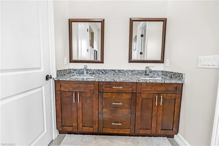 Double vanity with wood-finish cabinetry, integrated sinks, and granite countertops