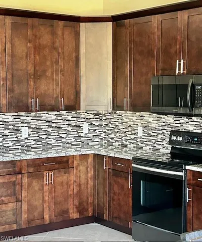 Kitchen featuring stainless steel appliances, light stone counters, dark wood finish cabinets, light tile patterned floors, and backsplash