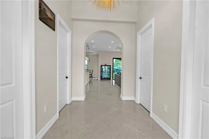 Polished tile flooring extending through a hallway with white paneled doors, an arched entryway, and a contemporary ceiling fixture