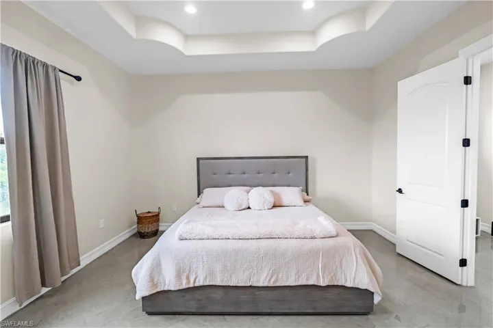 Bedroom featuring a tray ceiling with recessed lighting, light-toned walls, and wood-finish flooring