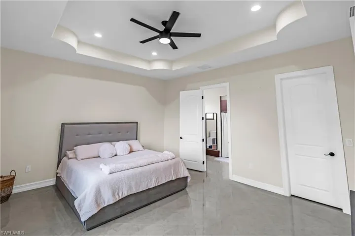 Recessed lighting illuminating a tray ceiling with a contemporary ceiling fan, light-toned walls, and grey-toned tile flooring