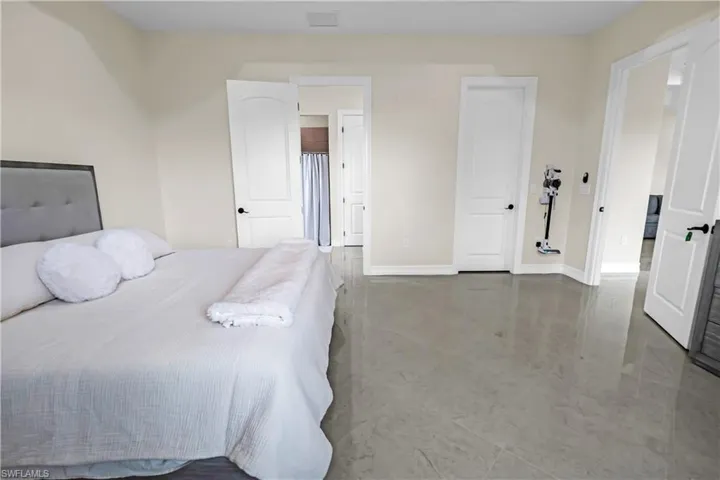 Spacious room featuring light-toned walls, high ceilings, polished tile flooring, and multiple white panel doors with black hardware