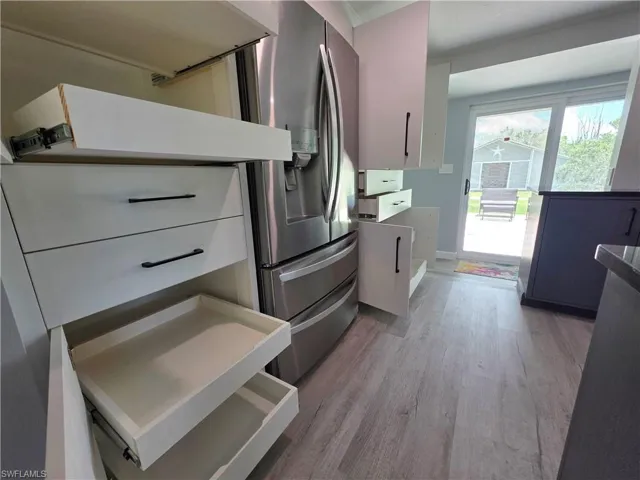 Kitchen with light wood-style flooring, stainless steel fridge with ice dispenser, and white cabinetry