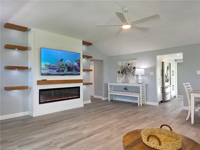 Living room featuring a ceiling fan, wood finished floors, lofted ceiling, and a glass covered fireplace