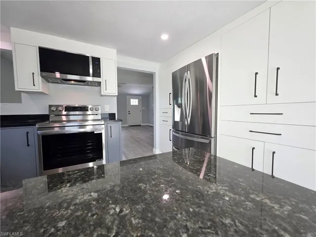 Kitchen with appliances with stainless steel finishes, dark stone counters, white cabinetry, wood finished floors, and recessed lighting