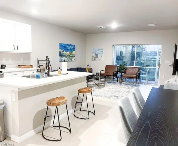 Kitchen featuring light countertops, white cabinetry, light tile patterned floors, a breakfast bar area, and a kitchen island with sink