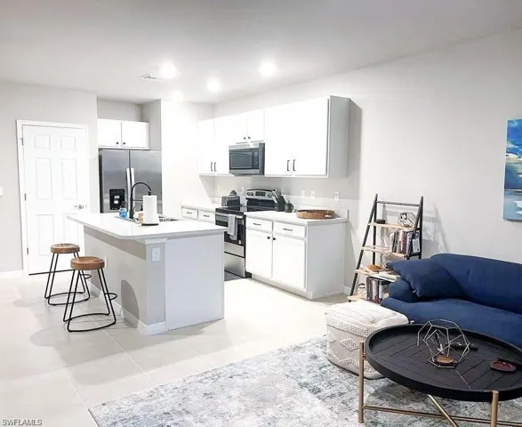 Kitchen featuring appliances with stainless steel finishes, a breakfast bar area, a center island with sink, white cabinets, and light tile patterned floors