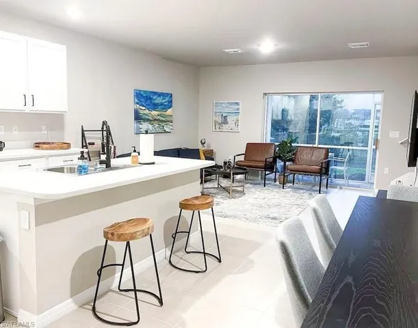 Kitchen featuring light countertops, a breakfast bar area, light tile patterned floors, white cabinetry, and an island with sink