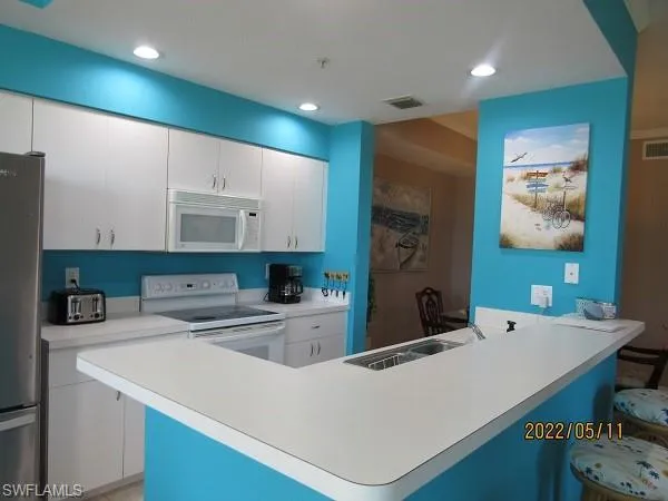 Kitchen featuring white appliances, a breakfast bar area, a peninsula, white cabinetry, and recessed lighting