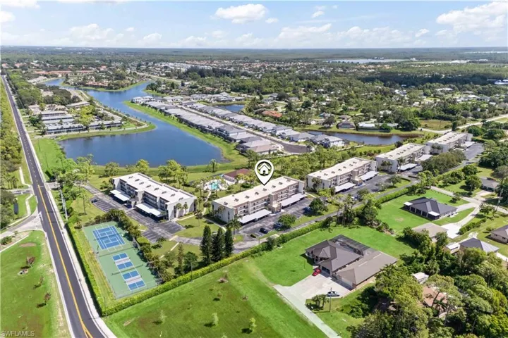 Stunning aerial view of the community featuring beautifully landscaped grounds, tennis courts, and a resort-style pool nestled by the lake.