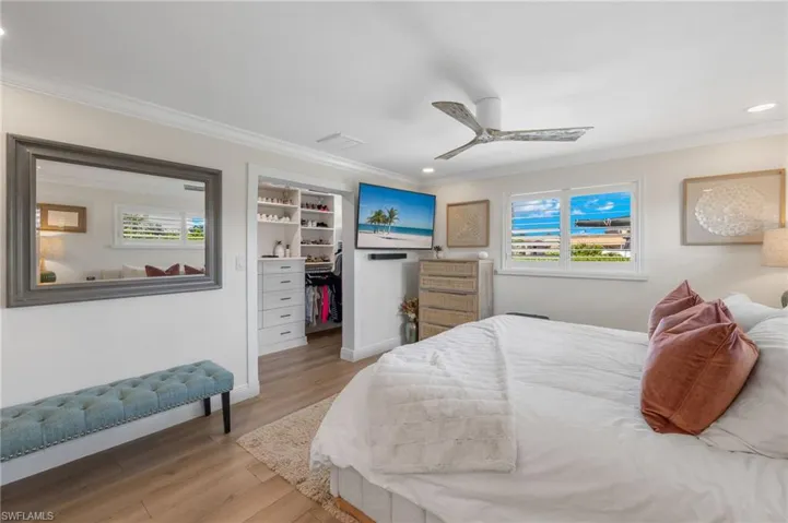 Bedroom with a walk in closet, ornamental molding, baseboards, light wood-style floors, and ceiling fan