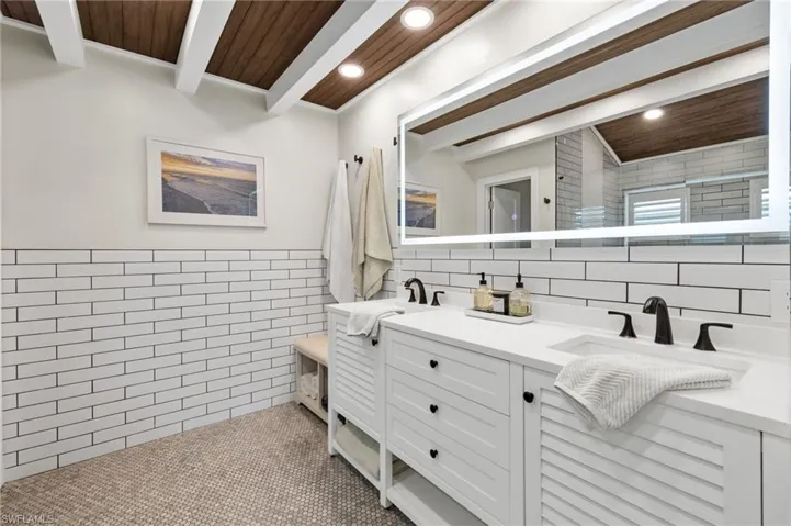 Bathroom with tile walls, a sink, double vanity, beamed ceiling, and recessed lighting