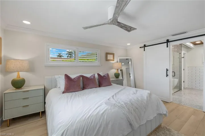 Bedroom featuring a barn door, visible vents, light wood-style floors, ornamental molding, and recessed lighting