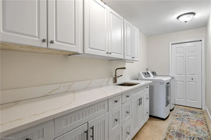 Clothes washing area with washing machine and clothes dryer, a sink, cabinet space, and light tile patterned floors