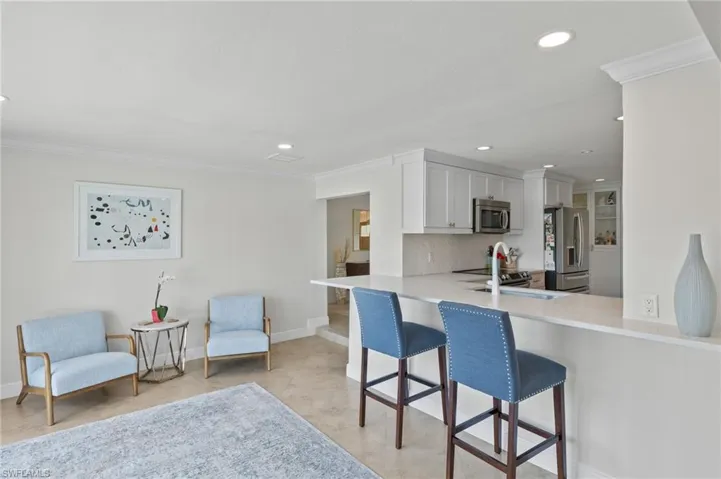 Kitchen featuring light countertops, crown molding, a kitchen bar, stainless steel appliances, and backsplash