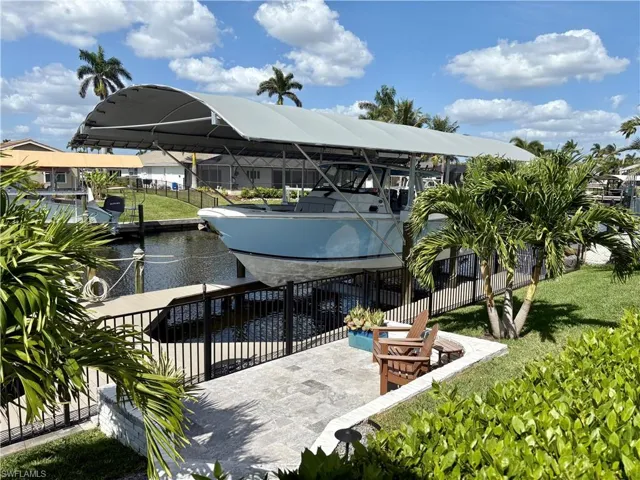 View of dock with boat lift, a water view, fence, and a lawn