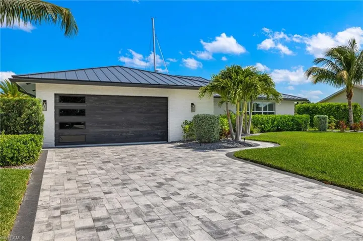View of front of house featuring metal roof, decorative driveway, a front yard, brick siding, and a standing seam roof