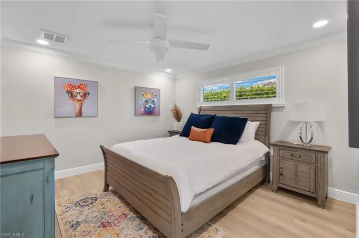 Bedroom with light wood-style flooring, crown molding, baseboards, and visible vents