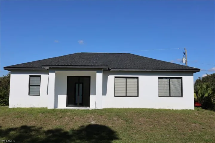 Rear view of property featuring a lawn, roof with shingles, and stucco siding