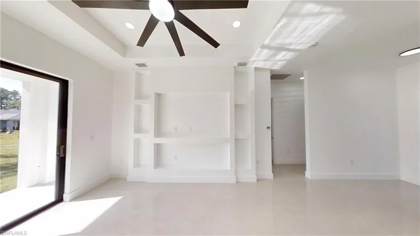 Empty room with recessed lighting, ceiling fan, a tray ceiling, and built in shelves