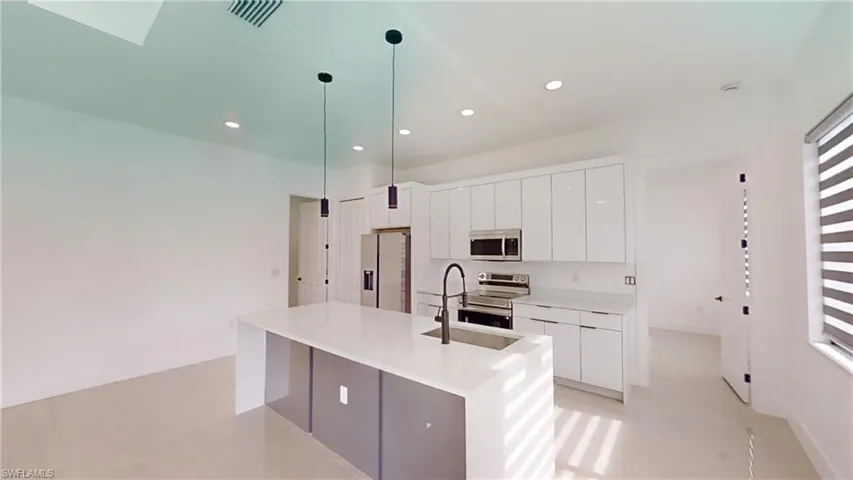 Kitchen featuring white cabinetry, stainless steel appliances, a kitchen island with sink, light stone counters, and modern cabinets