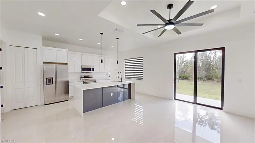 Two tone kitchen with stainless steel appliances, light stone countertops, a center island with sink, modern cabinets, and decorative light fixtures
