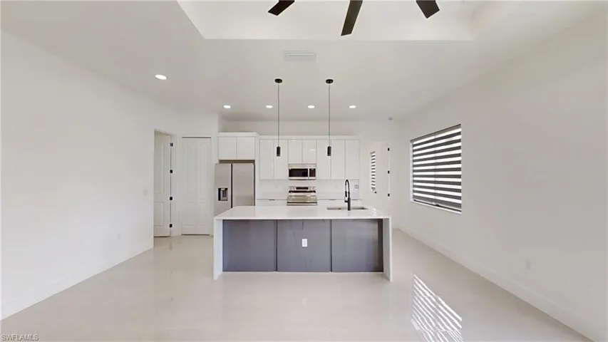 Kitchen featuring white cabinets, stainless steel appliances, a large island with sink, pendant lighting, and light stone countertops