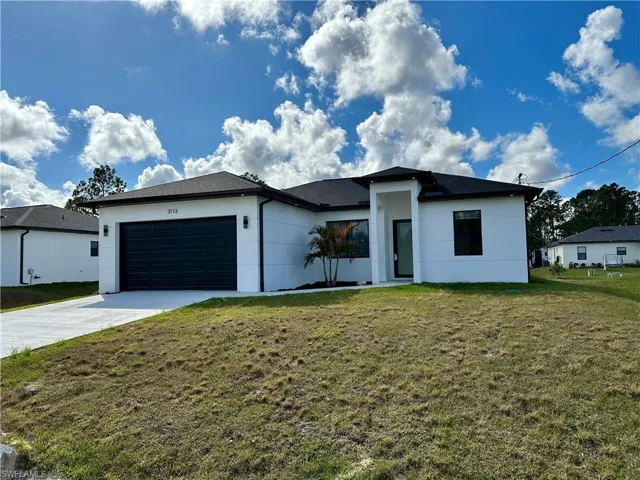 View of front of property with a front lawn, an attached garage, concrete driveway, and stucco siding