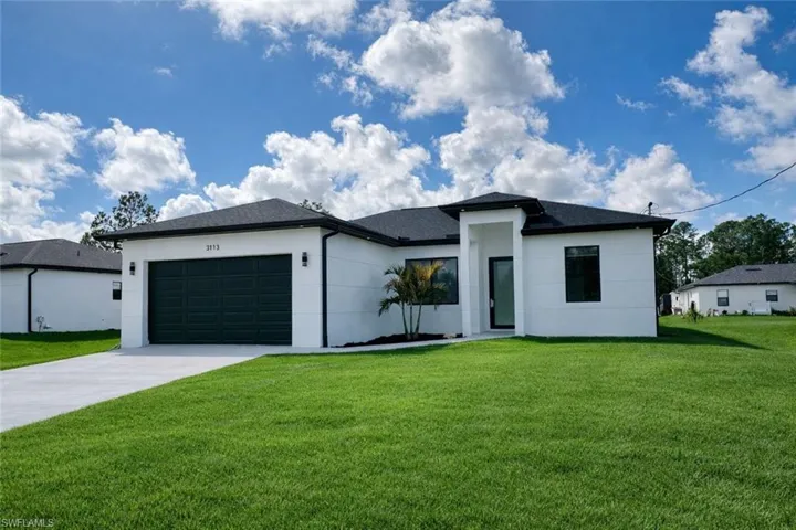 View of front facade (Edited grass) featuring a front yard, a garage, driveway, stucco siding, and a shingled roof