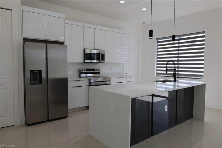 Kitchen with stainless steel appliances, a kitchen island with sink, white cabinetry, light stone countertops, and light tile patterned flooring