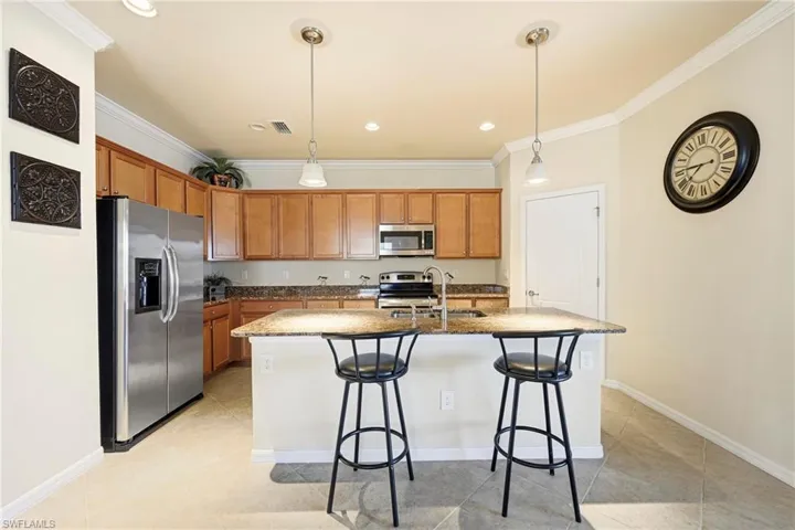 Kitchen with stainless steel appliances, wood finish cabinetry, an island with sink, hanging light fixtures, and crown molding