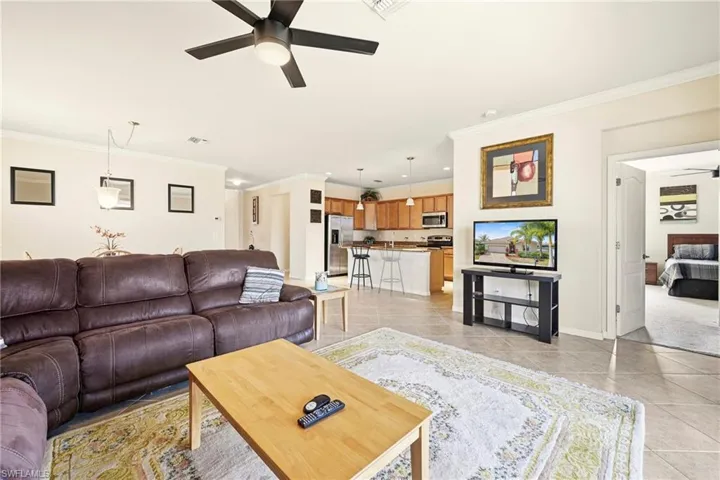 Living room featuring ceiling fan, crown molding, and light tile patterned flooring