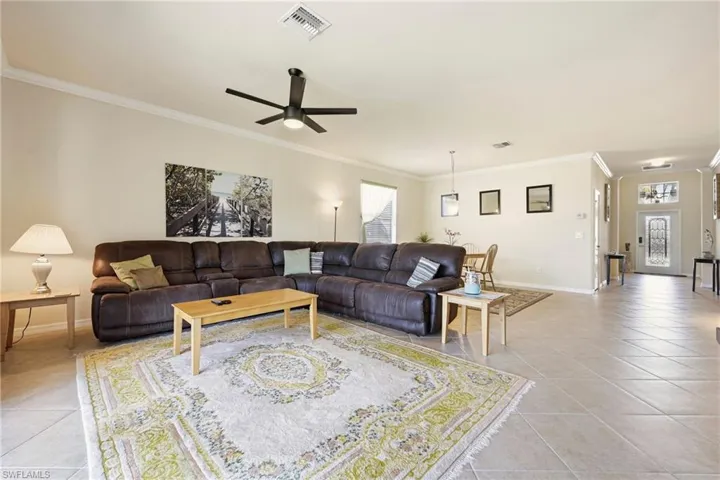 Living room featuring ornamental molding, a ceiling fan, and light tile patterned floors