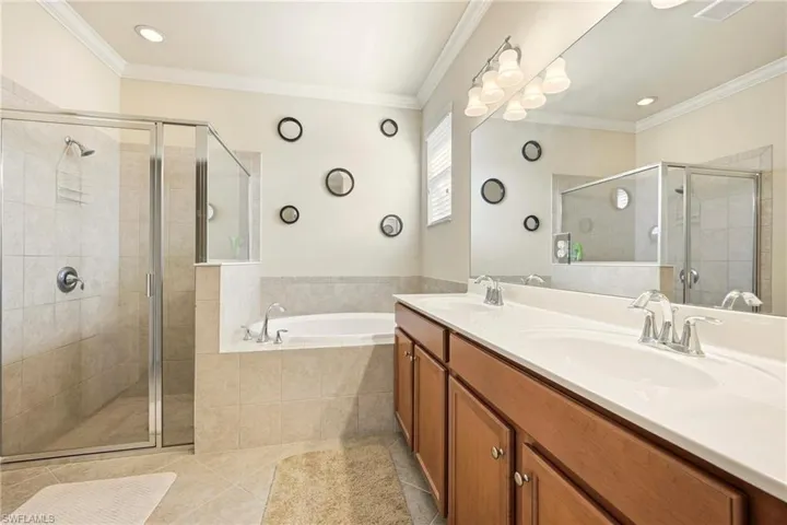 Bathroom featuring crown molding, double vanity, a stall shower, a bath, and light tile patterned floors