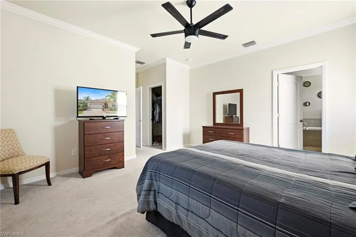 Bedroom with light carpet, ornamental molding, a spacious closet, and ceiling fan