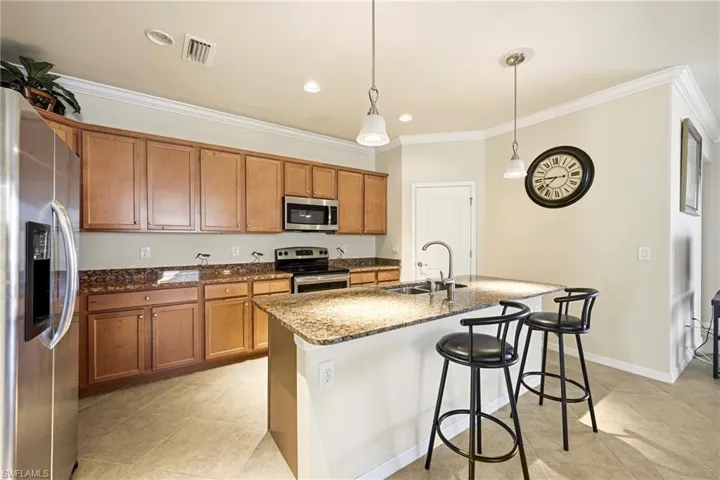 Kitchen with wood finish cabinetry, dark stone countertops, stainless steel appliances, a breakfast bar, and pendant lighting