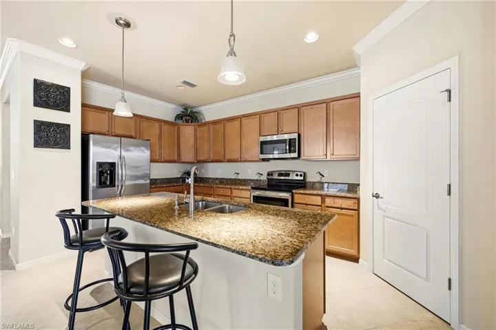 Kitchen with a breakfast bar area, wood finish cabinets, stainless steel appliances, hanging light fixtures, and a center island with sink