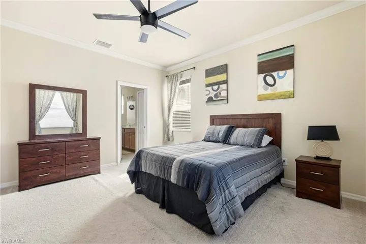 Bedroom with ornamental molding, connected bathroom, light carpet, and ceiling fan