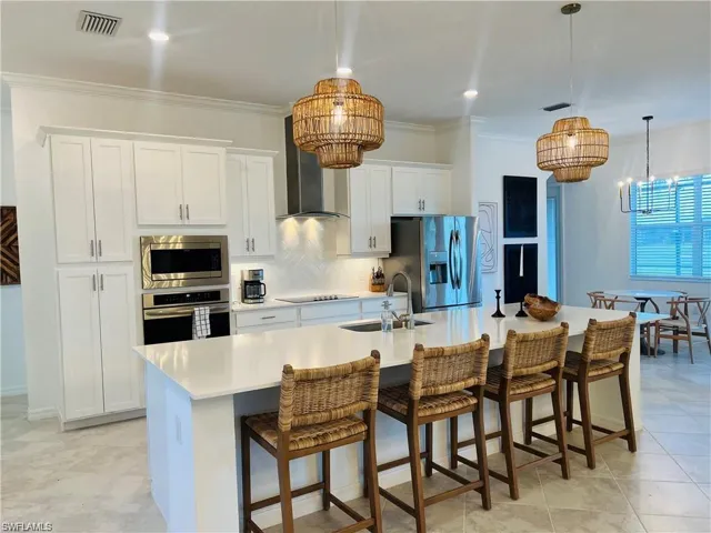 Kitchen featuring wall chimney exhaust hood, sink, a kitchen island with sink, and appliances with stainless steel finishes