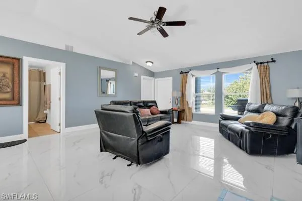 Living room featuring light marble finish floors, vaulted ceiling, and a ceiling fan