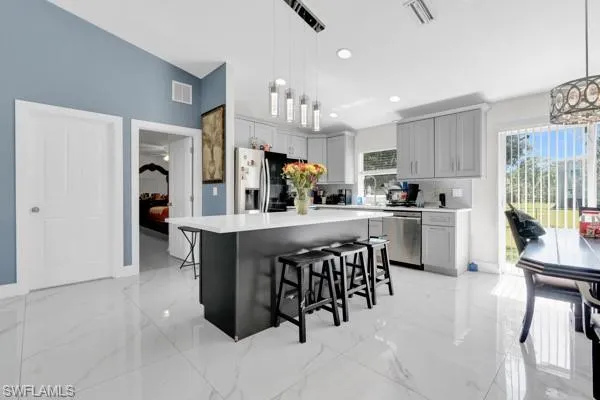 Kitchen with a kitchen bar, decorative light fixtures, light marble finish flooring, a kitchen island, and plenty of natural light