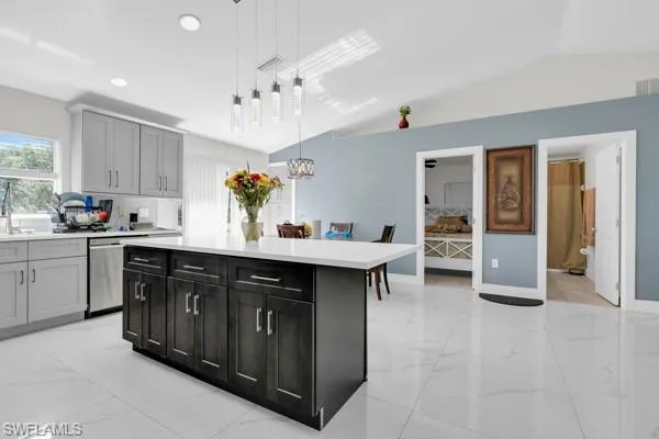 Kitchen with a center island, light marble finish flooring, hanging light fixtures, lofted ceiling, and dishwasher