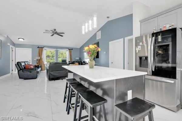 Kitchen featuring stainless steel fridge, a breakfast bar, light marble finish floors, a kitchen island, and lofted ceiling