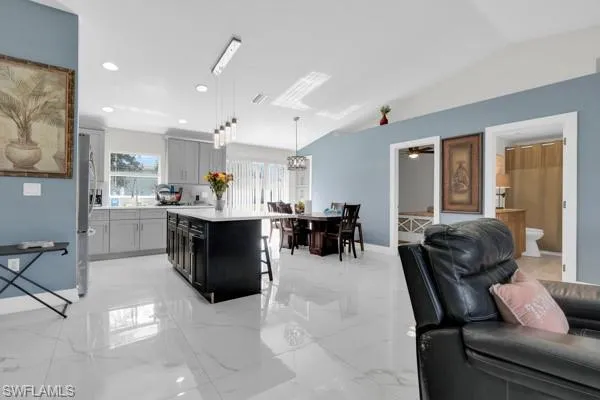 Kitchen with pendant lighting, a kitchen island, a kitchen breakfast bar, recessed lighting, and light marble finish floors