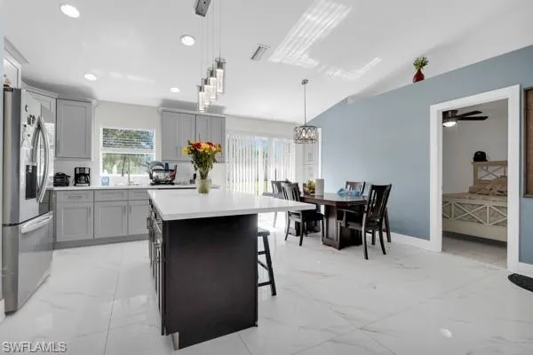 Kitchen with light marble finish floors, a breakfast bar, stainless steel fridge with ice dispenser, pendant lighting, and a center island