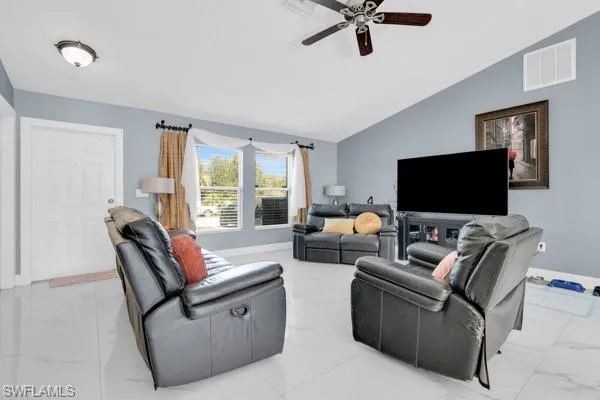 Living area featuring vaulted ceiling, light marble finish flooring, and ceiling fan