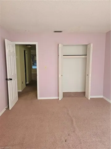 Unfurnished bedroom featuring light colored carpet, a textured ceiling, and a closet