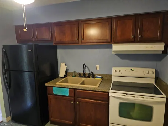 Kitchen featuring white electric stove, black fridge, and sink