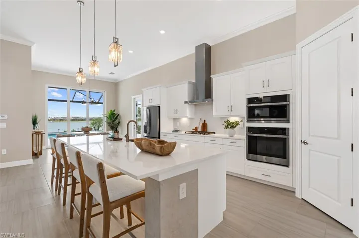 Kitchen featuring appliances with stainless steel finishes, a center island with sink, white cabinets, a kitchen bar, and wall chimney exhaust hood