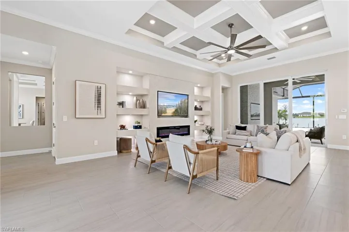 Living room with a large fireplace, coffered ceiling, ceiling fan, crown molding, and built in shelves
